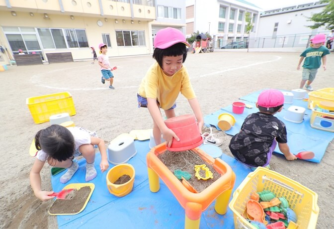 園庭でままごと遊びをする子供たち